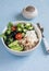 Mediterranean quinoa bowl with avocado, cucumbers, olives, tomatoes, feta cheese, arugula. On a blue background.