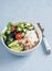 Mediterranean quinoa bowl with avocado, cucumbers, olives, tomatoes, feta cheese, arugula. On a blue background.