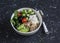 Mediterranean quinoa bowl with avocado, cucumbers, olives, tomatoes, feta cheese, arugula. On a dark background.