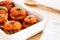 Mediterranean stuffed tomatoes with meat, bread crumbs, and herbs in a white dish, aside a white napkin and a spoon on oak