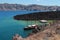 Mediterranean view: ships stand in a bay among black volcanic rocks, blue green sea water, mountains in the distance,