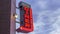 A medium 4K timelapse shot of a neon diner sign pointing to a cafe illuminated red in front of beautiful afternoon clouds