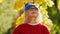 Medium closeup millennial blond curly-haired woman in a blue cap and glasses, looks up park background copy space