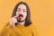 Medium closeup young long-haired man touching fake black moustache yellow background copy space isolated studio shot