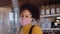 Medium eye shot of Female African coffee shop owner wearing face visor standing behind of counter and Sneeze Guard