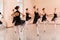 Medium group of teenage girls in black dresses practicing ballet moves in a large dance studio