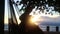 Medium POV of person`s feet and legs in a hammock as they swing moderately in the setting sun by the sea.