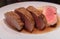 medium rare roasted pork fillet with a wine and balsamico sauce, cut into tasty slices and put on a white plate.