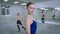 Medium shot of confident charming slim ballerina looking at camera smiling with ballet dancers dancing at barre in