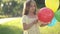 Medium shot front view of brunette Caucasian girl with brown eyes posing in sunshine with colorful balloons. Cute child