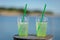 Medium shot of a glass filled to the top green drinking liquid with ice cubes,two straws with blurred ocean background