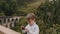 Medium shot happy cute little European boy taking smartphone photo at Ella Nine Arches Bridge on Sri Lanka vacation.