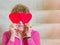 Medium shot of middle aged Caucasian woman holding red paper hearts over her eyes while sitting on carpeted stairs