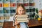 Medium shot portrait of adorable elementary child school girl holding stack of books in library at school looking at