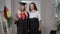 Medium shot portrait glad Caucasian mother and daughter in graduation outfit posing with German flag at home. Happy