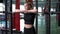 Medium shot portrait of young fit slim Caucasian woman standing in gym at barbell stand looking away. Thoughtful