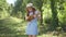 Medium shot redhead teenage girl in blue dress and straw hat playing ukulele standing in sunshine in spring park