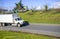 Medium size and duty semi truck transporting commercial cargo in long box trailer driving on the city road between green hills