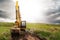 Medium size yellow excavator working in a green field. Building family house or farm in a country side concept. Dramatic cloudy