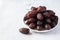 Medjoul dates in a white plate and glass of water on a gray background. Close up