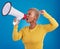 Megaphone, black woman and screaming in studio with fist of power, broadcast or vote on blue background. Speaker