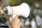Megaphone in hand of old woman on blurred background. Real elderly activist makes speech using loudspeaker. Copy space