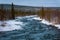 Melting snow and flowing cold blue river in the snow next to the forest. Arrival of spring