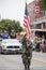 Member of Cherokee Honor Guard in camos presents American Flag in parade while tribe elders in Mustang