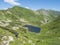 Men hiker walking down to Beautiful vivid blue mountain lake Horne Jamnicke pleso with green mountain peaks view from