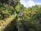 Men hiker walking on footpath along Lavada - water irrigation canals covered by moss and lush vegetation on hiking trail