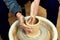 The men potters hands form by a clay pot on a potters wheel. The potter works in a workshop.