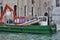 Men replace dock pilings from aboard a work boat on a canal in Venice