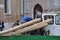 Men replace dock pilings from aboard a work boat on a canal in Venice