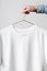 Men`s Crew Neck T-Shirt Mock-Up - Man holding a white t-shirt on a copper wire clothes hanger