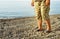 Men& x27;s feet in flip-flops and shorts, a man standing on the beach on a pebble beach, sunrise in the morning