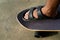 Men`s feet In sandals, stepping on a black Surf Skate on the sand in the park