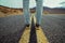 Men`s feet standing on asphalt desert road with yellow marking lines. Man wearing sneakers and jeans.