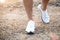 Men`s feet in white sneakers running over rough terrain. Cross country running with focus on runner`s legs
