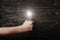 Men`s fist with luminous lightbulb on dark wooden background. The concept of bold ideas
