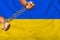 Men`s hands chained in heavy iron chains against the background of the flag of Ukraine on a gentle silk with folds in the wind,