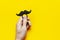 Men`s hands hold Black mustache, props for photo booths, carnival, parties on yellow background top view flat lay copy space