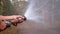 Men`s Hands Hold a Fire Hose from Which Water Runs under Pressure in Pine Forest