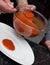 Men`s Hands Pouring Red Tomatoe or Chilly Sauce over Red Plate for Food Garnish. Ketchup Spill of Tomato sauce. Vertical