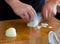 Men`s hands shred white onion on a wooden cutting board