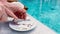 men's hands slice a white soft coconut with a knife on a plate by the swimming pool with blue water