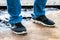 Men`s legs in blue jeans and black sneakers with white soles stand on a dirty oiled plywood board. Dirty car master workplace