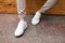 Men`s legs in leather fashion white sneakers in stylish beige pants. Trendy casual outfit. Details of everyday look.