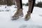 Men`s legs in stylish pants in fashionable brown winter leather shoes with yellow laces on the background of snow. Fashion.