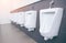 Men`s room with white porcelain urinals in line. Modern clean public toilets with tiles