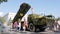 Men in uniforms walk in city among people near large military machine on street